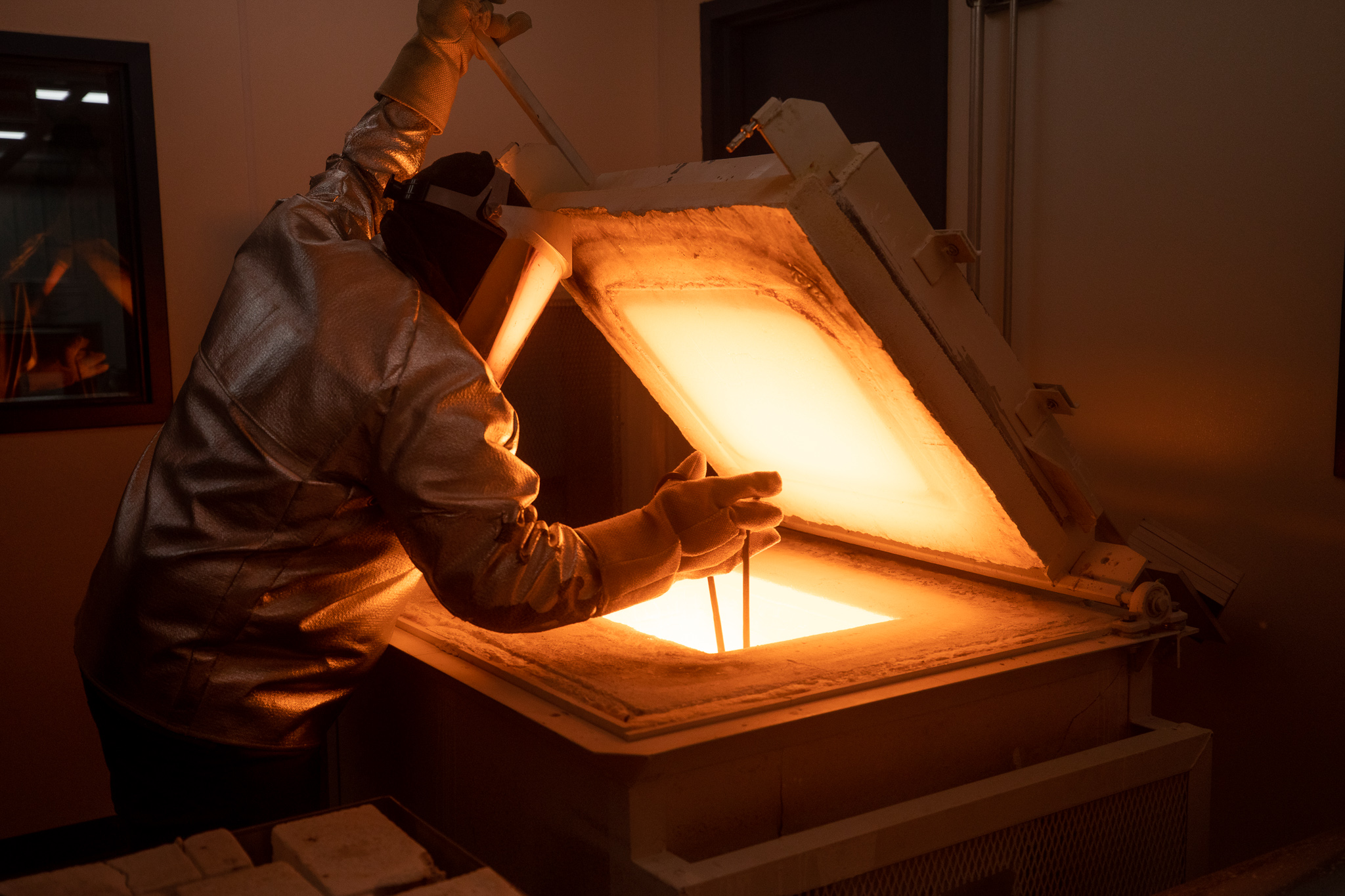 Worker in protective gear removing a crucible from a glass furnace